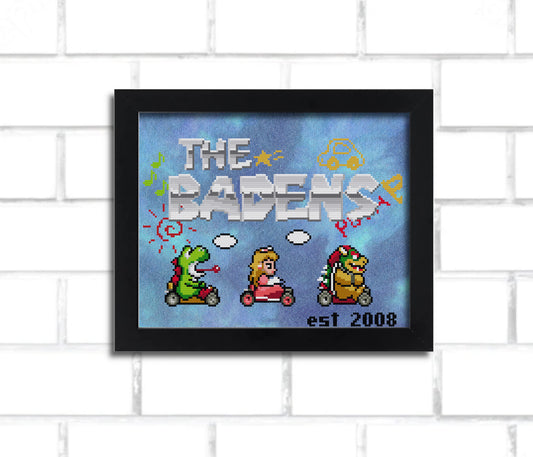 A digital render of a cross stitch, it says "the badens" ina metallic looking 8 bit mario-inspired font and features Super Mario Kart inspired sprites of Bowser, Peach, and Yoshi. it's in a black frame hung on a white brick wall.