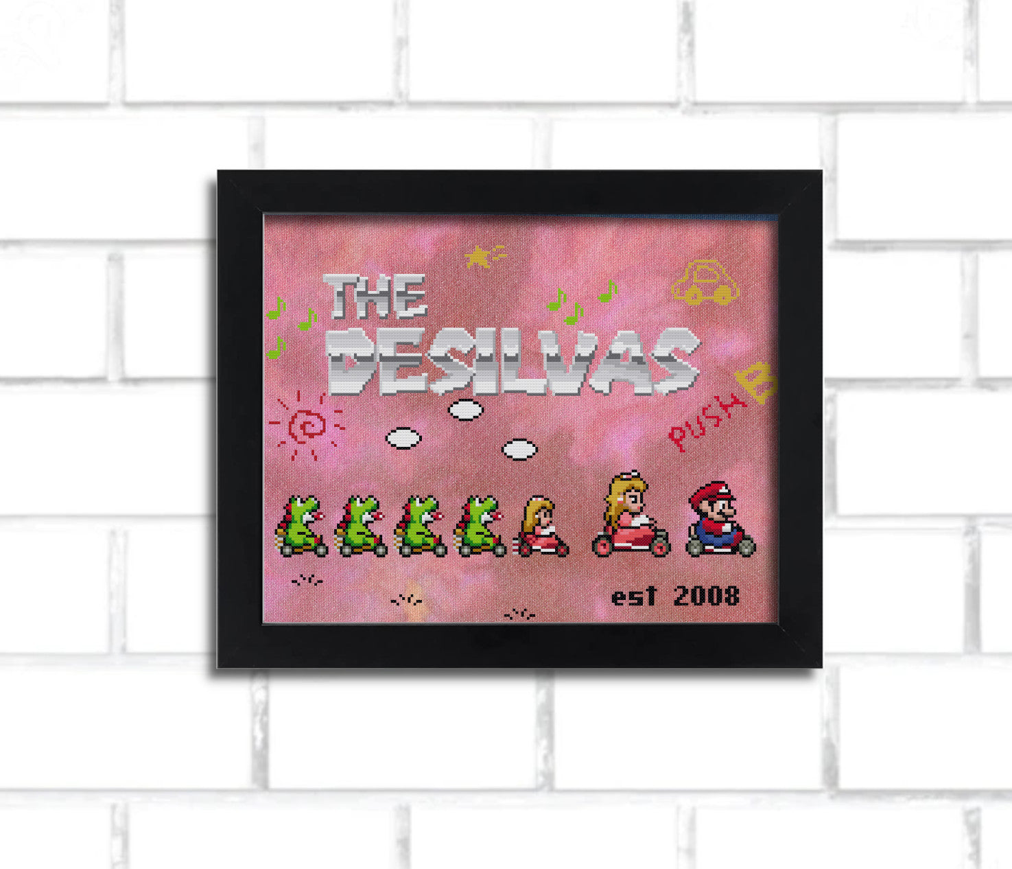 A digital render of a cross stitch, it says "the desilvas" in a metallic looking 8 bit mario-inspired font and features Super Mario Kart inspired sprites of Mario, peach, a small peach, and four small yoshis.. it's in a black frame hung on a white brick wall.