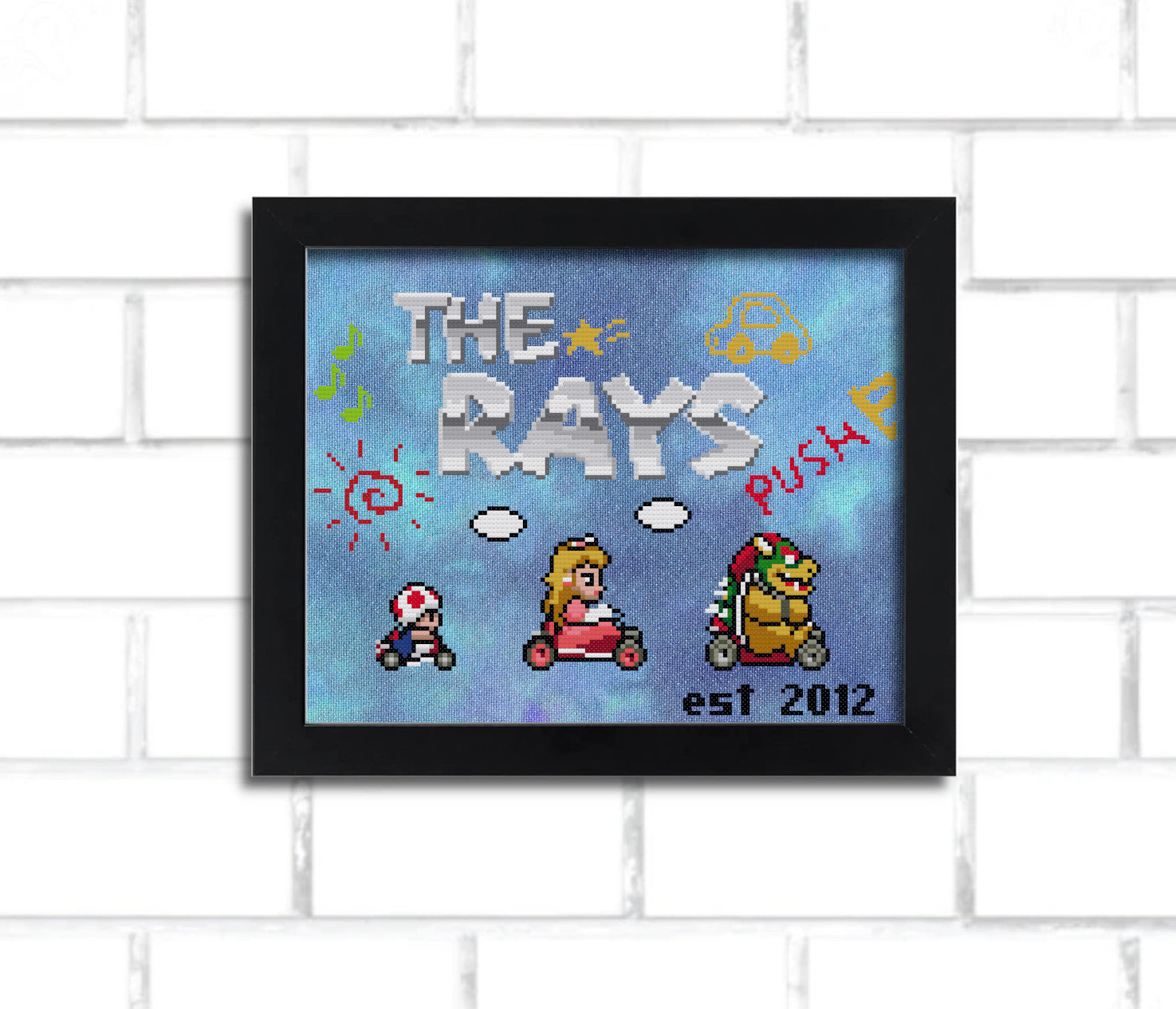 A digital render of a cross stitch, it says "the rays" in a metallic looking 8 bit mario-inspired font and features Super Mario Kart inspired sprites of Bowser, Peach, and small Toad. it's in a black frame hung on a white brick wall.