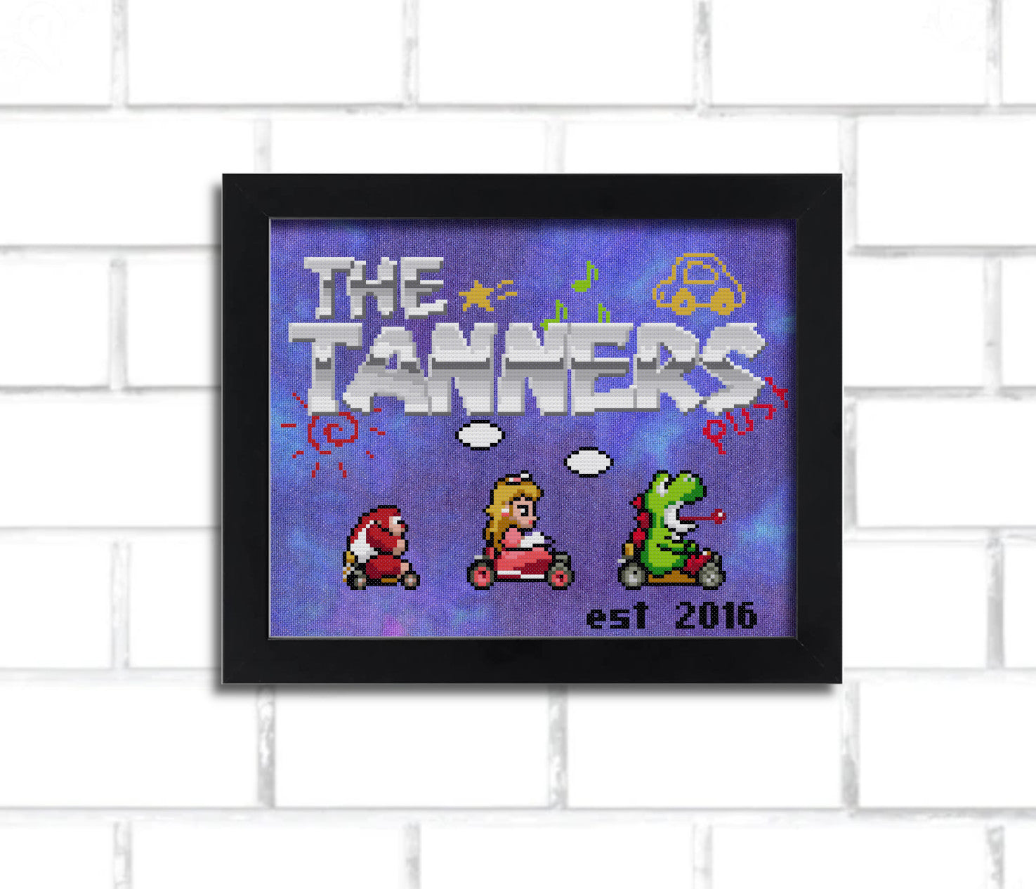 A digital render of a cross stitch, it says "the tanners" in a metallic looking 8 bit mario-inspired font and features Super Mario Kart inspired sprites of Yoshi, Peach, and small Donkey Kong. it's in a black frame hung on a white brick wall.